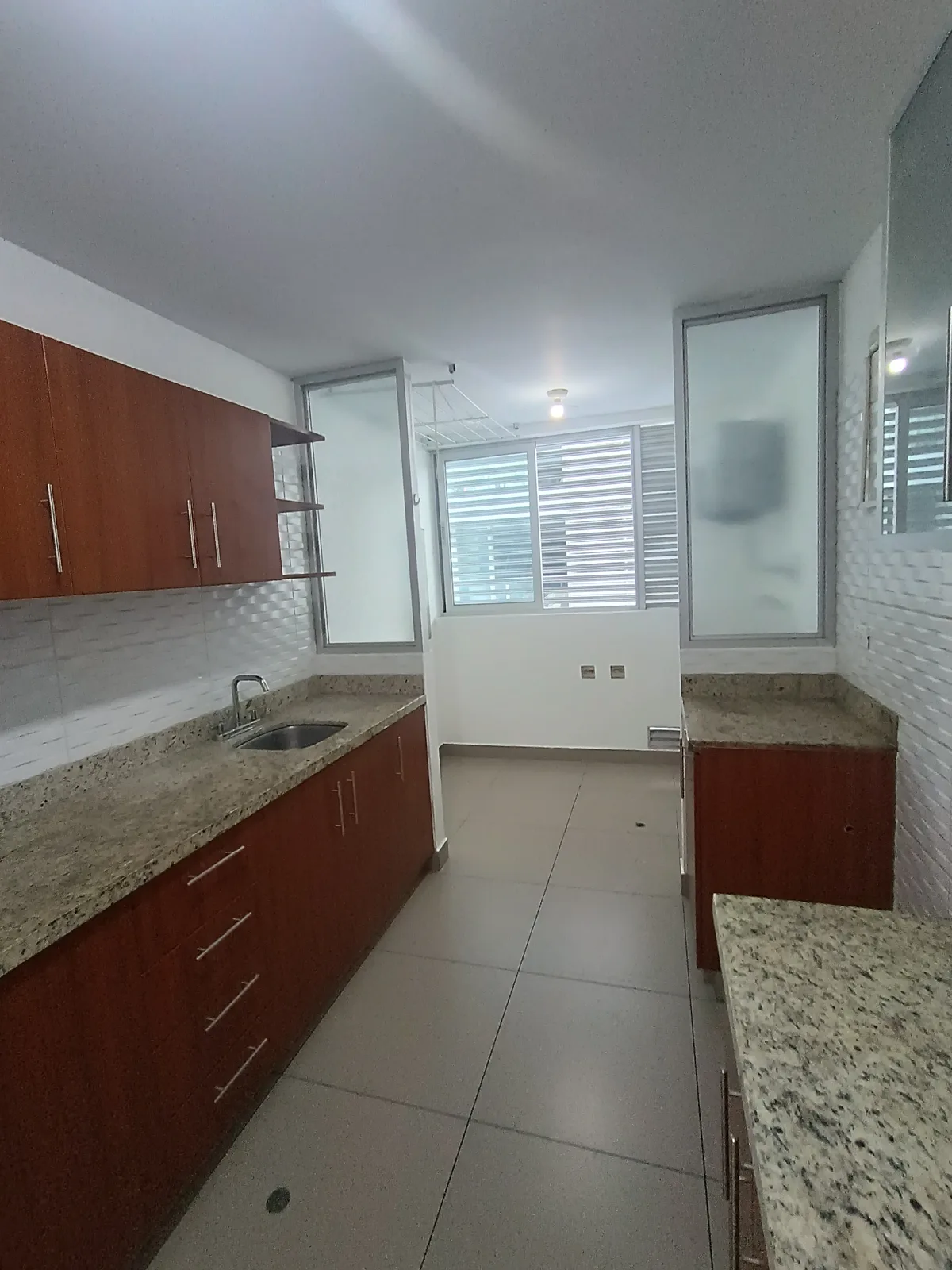 Cocina equipada con mesada de granito, muebles de madera y ventana con celosía
