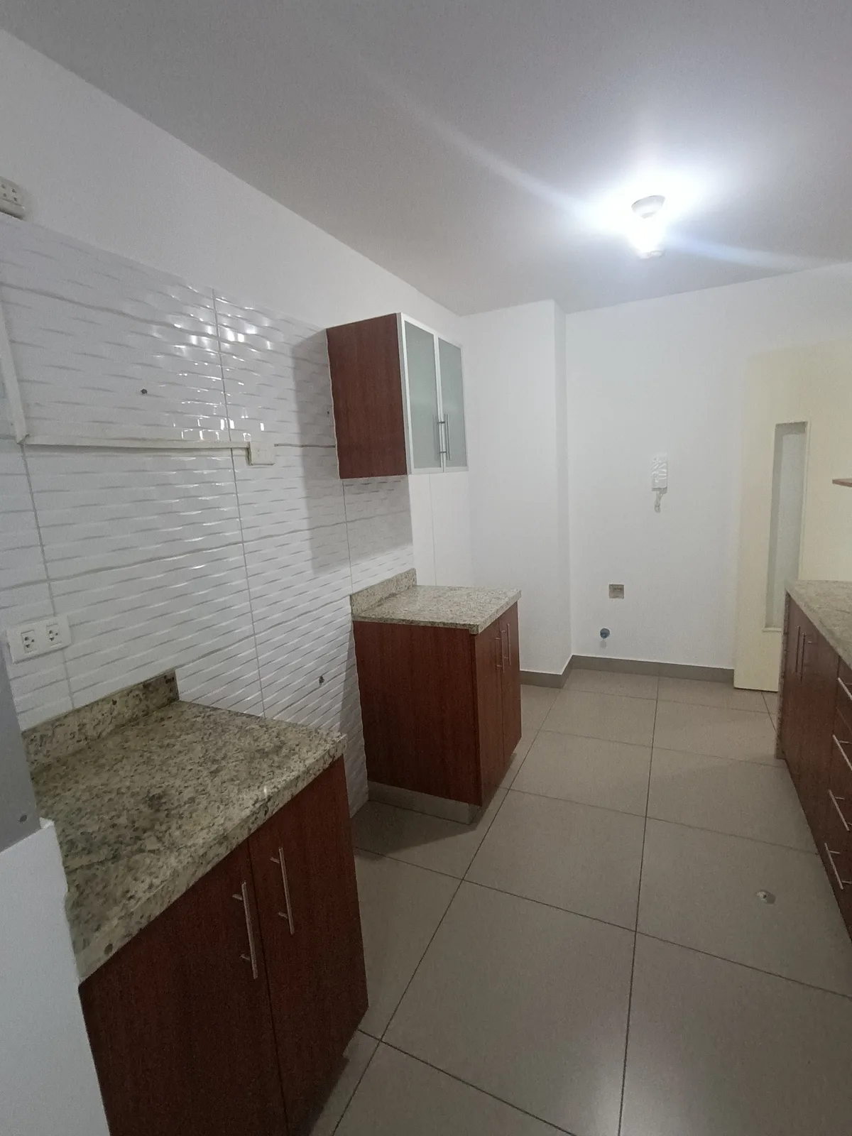 Cocina amplia con mesada de granito, muebles de madera y backsplash texturizado blanco