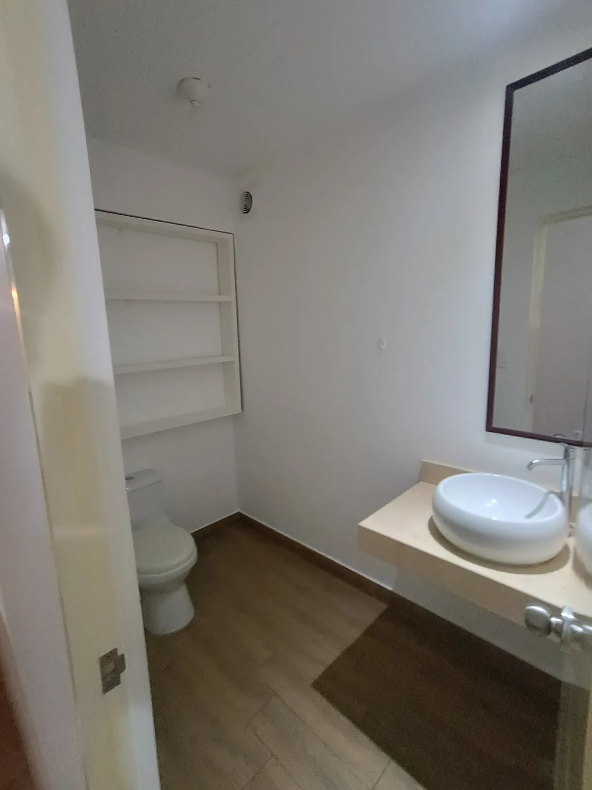 Baño secundario con bacha sobre mesada, espejo y estantería empotrada