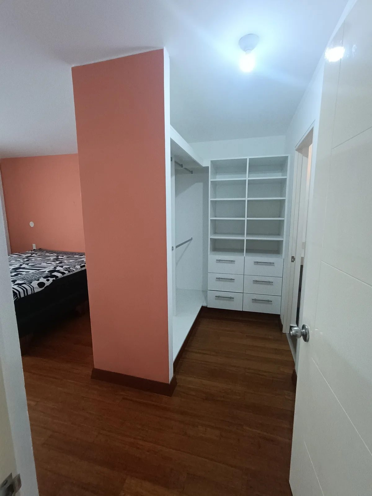 Vestidor blanco empotrado con estantes y cajones junto a muro de acento terracota