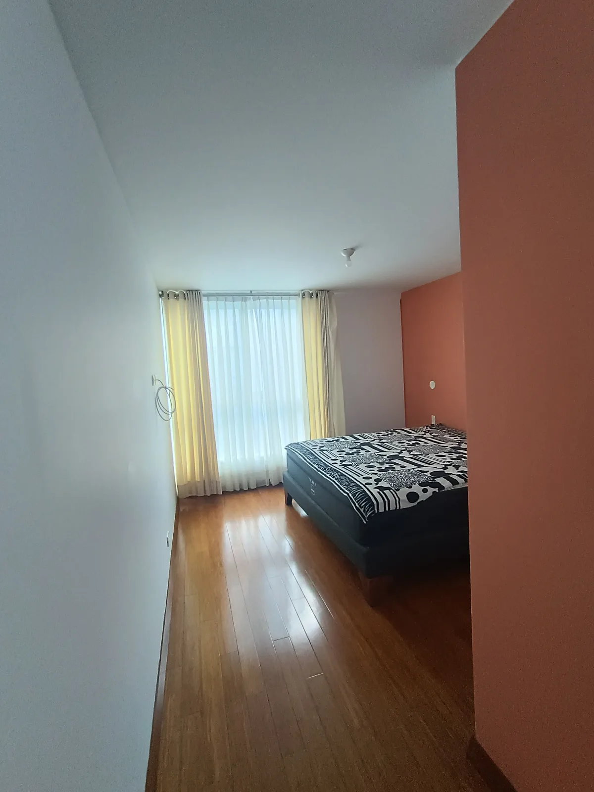 Dormitorio principal con muro de acento terracota y ventana grande con cortinas